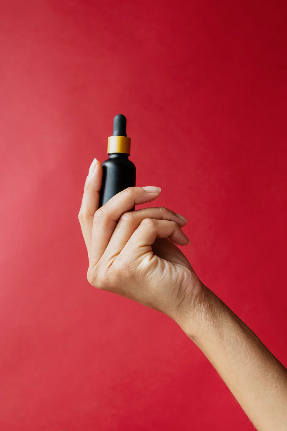 Hand holding the matte black Snoot dropper bottle against a red backdrop